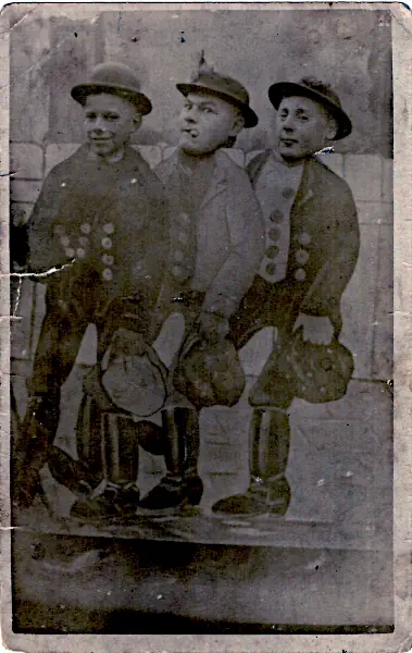 Drei Kameraden auf dem Volksfest (um 1900 bis 1930) Junge Männer bei einer Volksfest-Kulissenfotografie mit bemalter Jahrmarkts-Szenerie, Anfang des 20. Jahrhunderts.