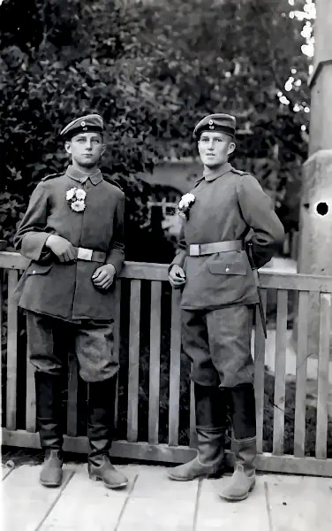 Zwei junge Soldaten mit Blumen posieren vor einem Gartenzaun.